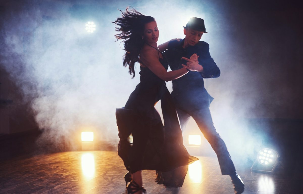 Skillful dancers performing in the dark room under the concert light and smoke