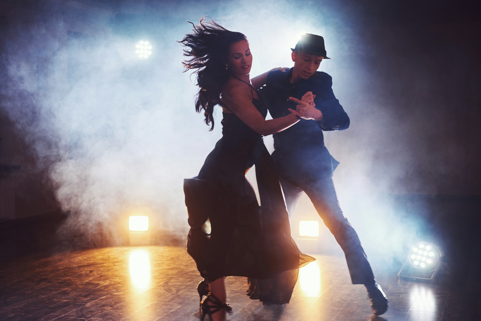 Skillful dancers performing in the dark room under the concert light and smoke