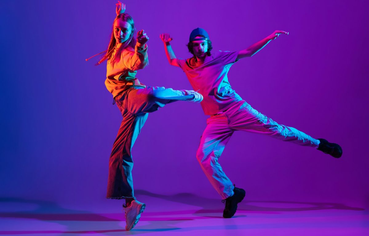 Two dancers, young man and woman dancing hip-hop in casual sports youth clothes on gradient purple