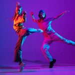 Two dancers, young man and woman dancing hip-hop in casual sports youth clothes on gradient purple