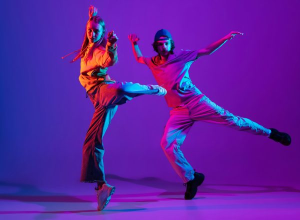 Two dancers, young man and woman dancing hip-hop in casual sports youth clothes on gradient purple