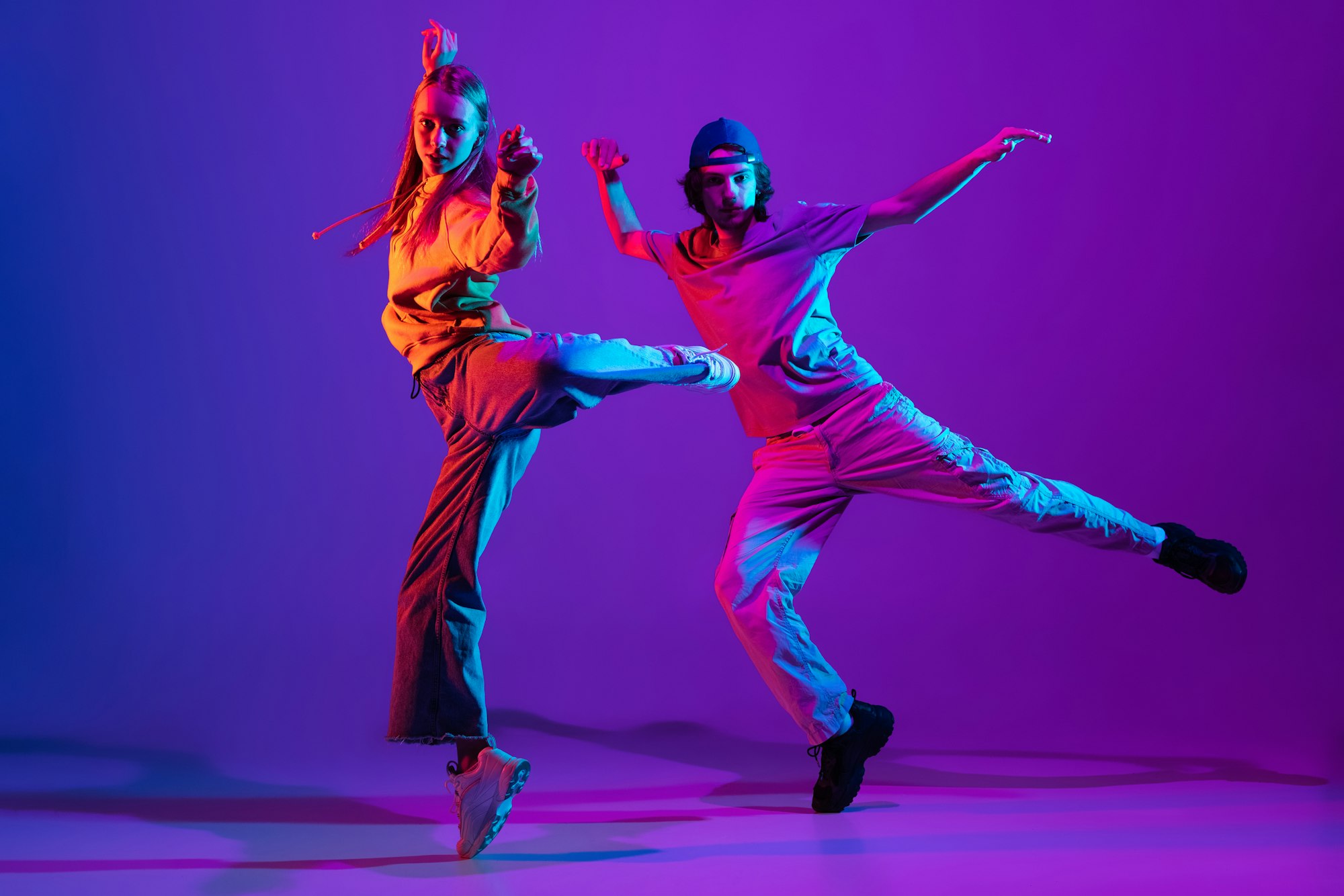 Two dancers, young man and woman dancing hip-hop in casual sports youth clothes on gradient purple